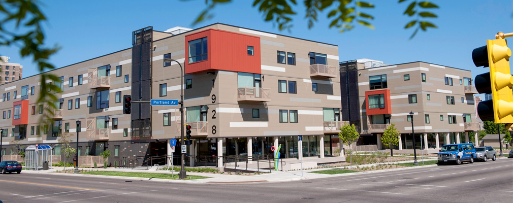 Photograph of the front and side façades of two 4-story residential buildings at a street intersection. 