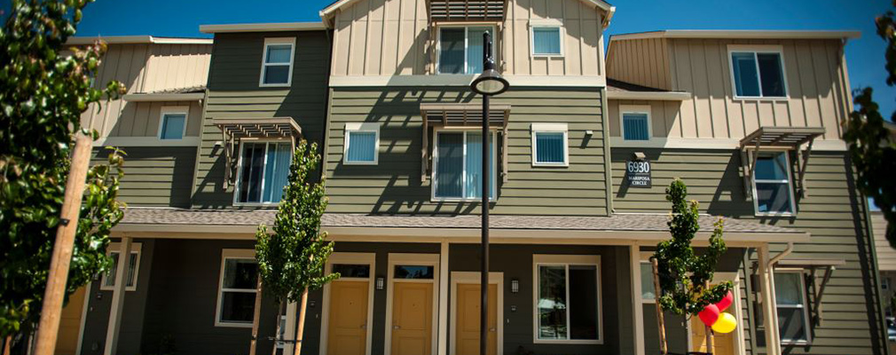 Photograph of the front façade of a three-story multifamily building with newly planted trees and shrubs in front of the building.