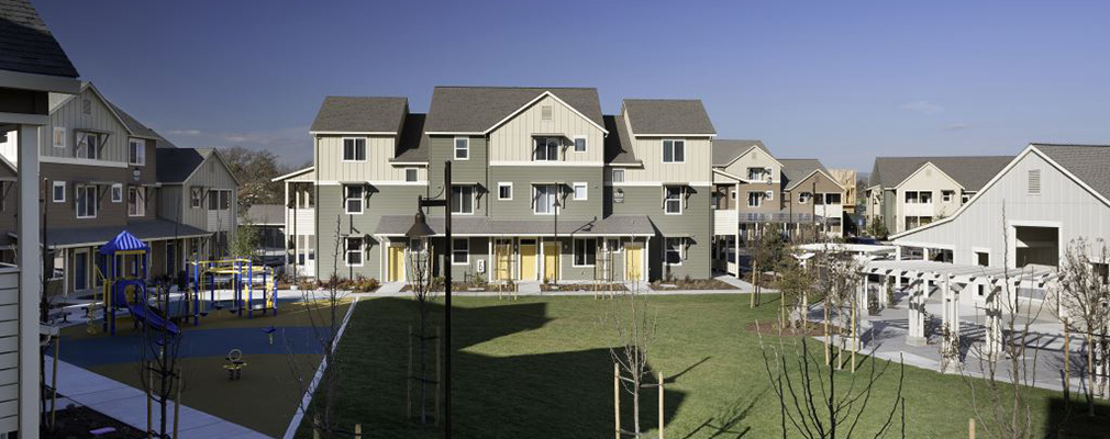 Photograph of a green space and small playground surrounded by multifamily buildings.