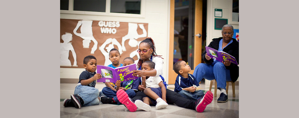 Photograph of five children and two adults sitting in a classroom reading books.