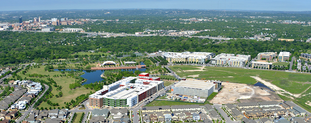 Low-angle aerial photograph of the Mueller Town Center under construction, with downtown Austin in the background.