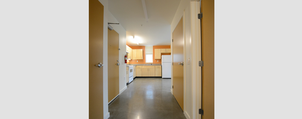 Photograph of the interior of an apartment showing a wide hall leading to the kitchen in the background.