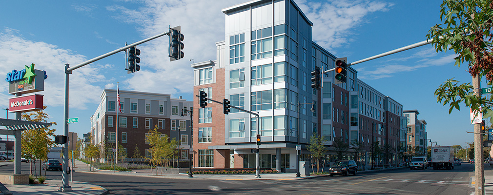 Photograph of a five-story mixed-use building on the corner of an intersection of a commercial street and a side street.