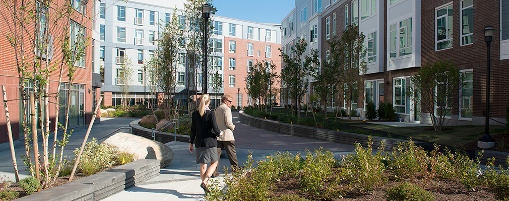 Photograph of two people walking in a courtyard with four- and five-story buildings on three sides.