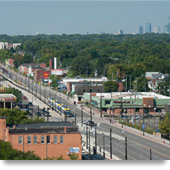 Aerial view of buildings, a main thoroughfare, and a light rail line and train running along the middle of the street.
