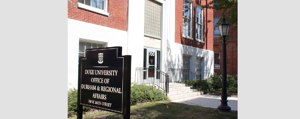 Photograph of a multistory brick institutional building with a sign in front reading, “Duke University Office of Durham & Regional Affairs.”