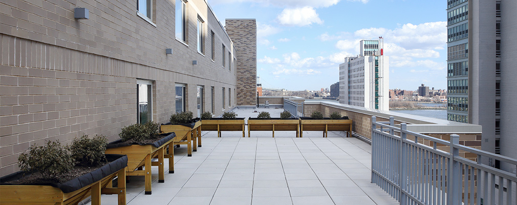 Photograph of the balcony two floors below the roof with six raised planter beds, with the East River in the background.