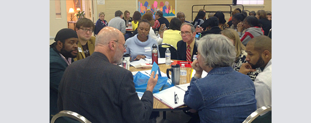 Photograph of people in conversation sitting at several round tables in a large meeting room.