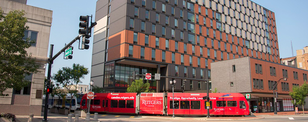 Photograph of 2 façades of a 12-story mixed-use building, with a tram passing in front of it.