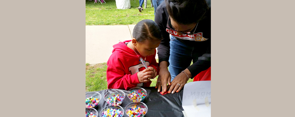 Photograph of a girl making a bracelet with help from an adult.