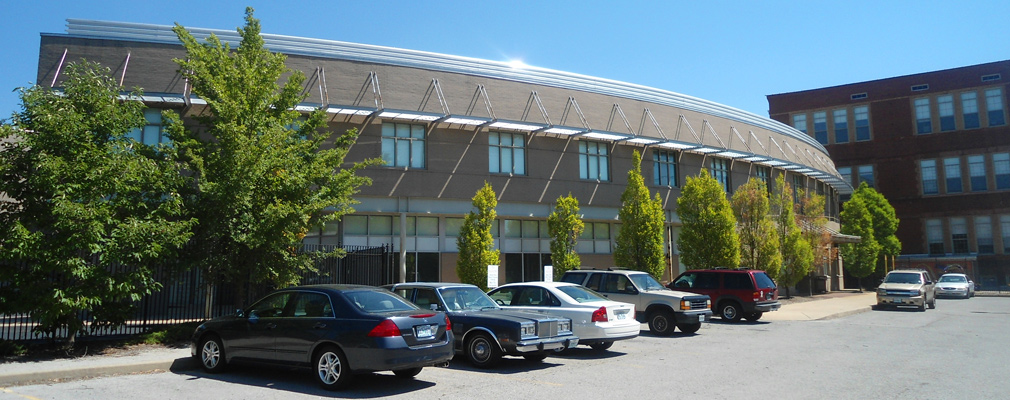 Photograph of the front façade of a two-story building with a line of trees and a parking lot in the foreground.