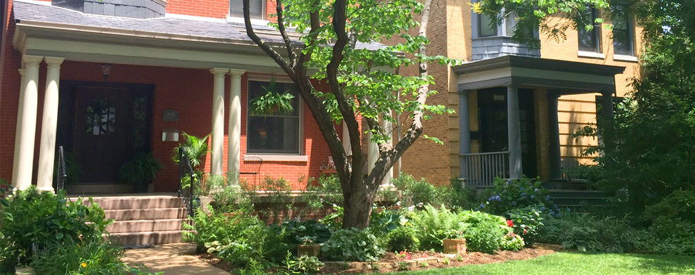 Photograph of two historic, two-story, brick single-family houses featuring porches and landscaped yards.