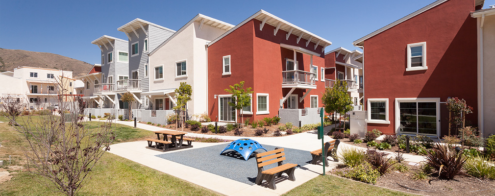 Photograph of the common greenspace with play equipment, benches, and a picnic table.