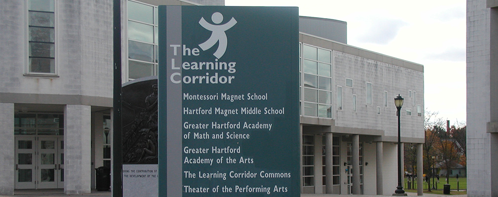 Photograph taken in a courtyard on the Learning Corridor campus highlighting a directional sign for seven facilities.