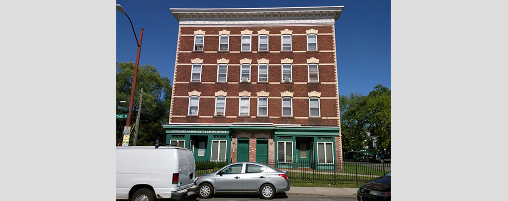 Photograph of the front façade of a four-story brick multifamily buildings.