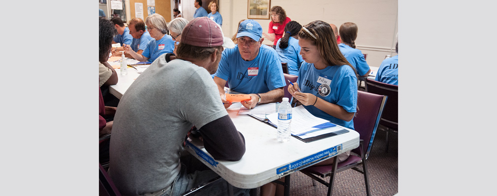 Photograph of VISTA volunteers and persons experiencing homelessness sitting at long rows of tables in a meeting room.