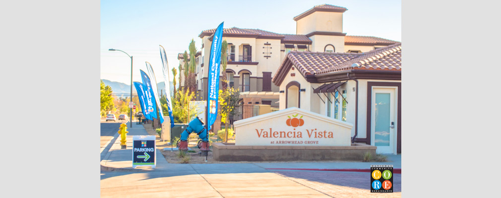 Photograph of a one-story community building with an entrance sign in the foreground and a three-story multifamily building in the background.