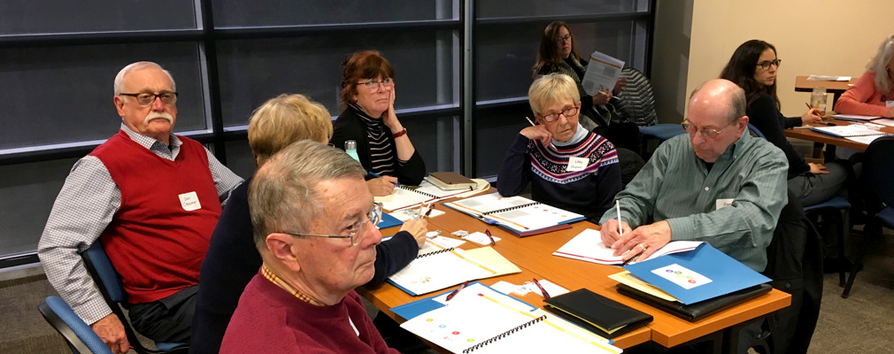 Photograph of eight people seated at tables in a meeting room.