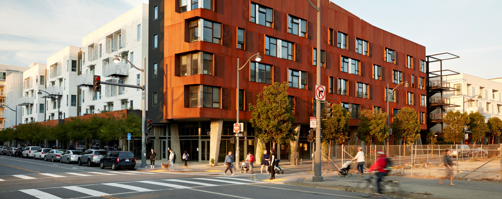 Photograph of two street façades of a five-story mixed-use building, with one side clad in weathering steel.
