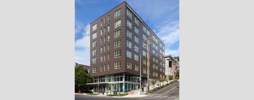 Photograph of two façades of a six-story apartment building on a street corner.