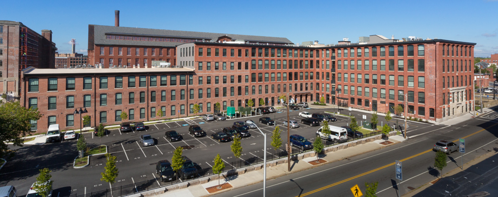 Photograph of an L-shaped brick mill building, with the building entrance at the right edge of the photograph.