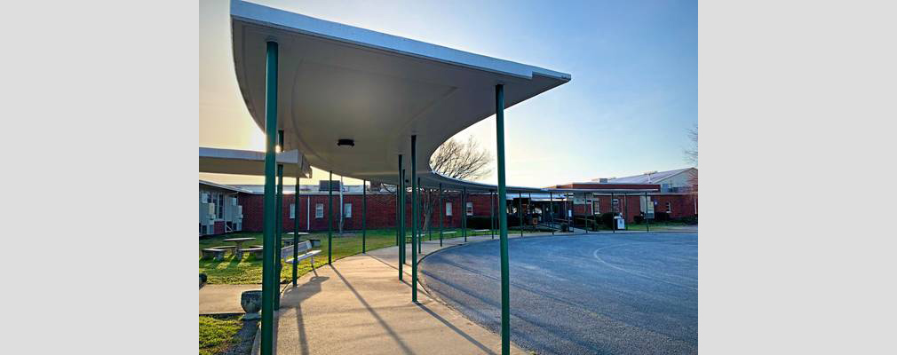 Photograph of the front façade of a one-story brick building with a covered walkway and lawn in front.