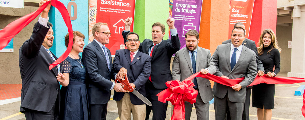 Photograph of 10 people at a ribbon-cutting ceremony in front of the Marydale Community Services Center, with banners in English and Spanish describing services available at the center.