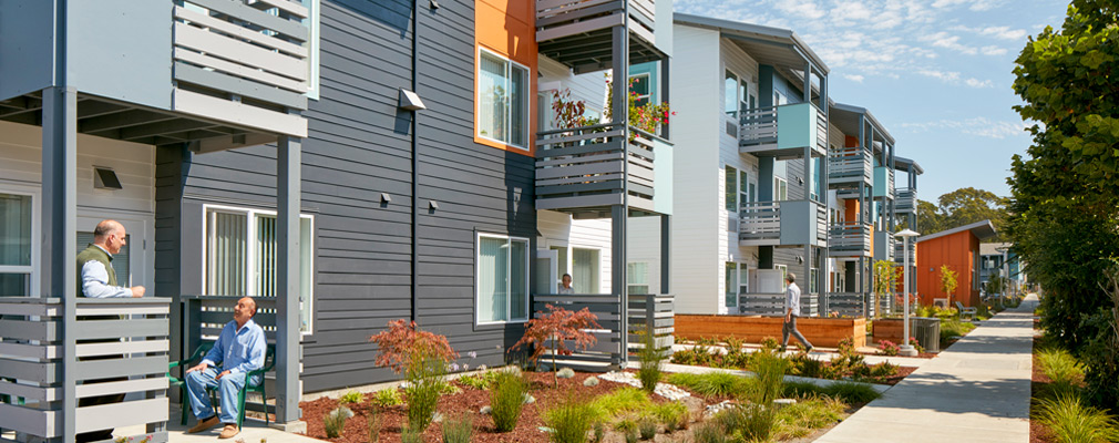 Photograph of the front façade of three-story apartment buildings with porches and balconies at entrances to the units.