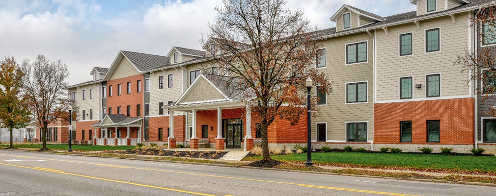 Photograph of the front façade of a three-story multifamily building, with a one-story nonresidential unit at the left end of the building.