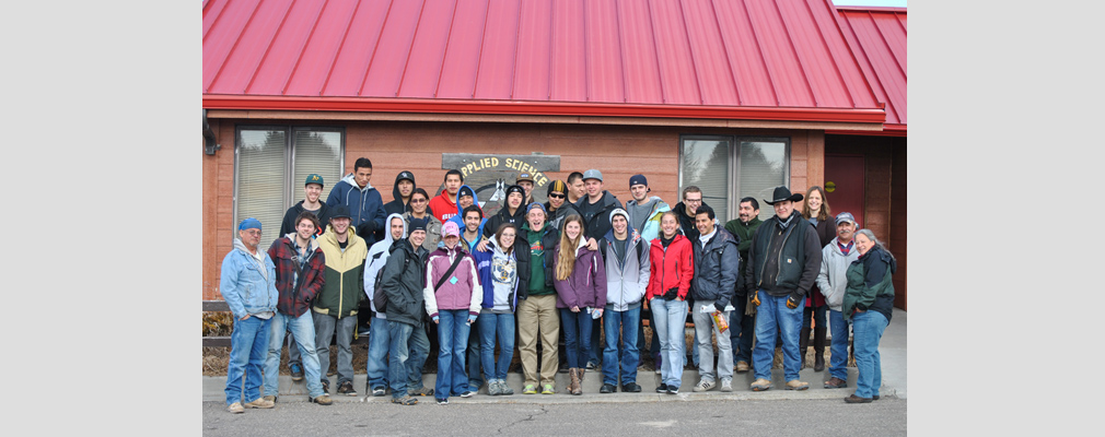 Photograph of a group of students and instructors posing in front of a one-story building on the campus of the Oglala Lakota College.