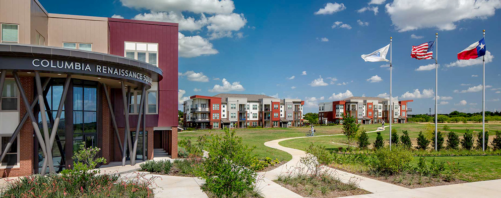 Photograph of a paved pathway leading from the entrance of a three-story apartment building in the foreground and two three-story apartment buildings in the background.