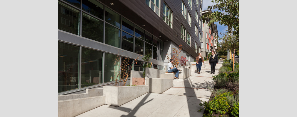 Photograph of three people on a sloping sidewalk next to an apartment building.