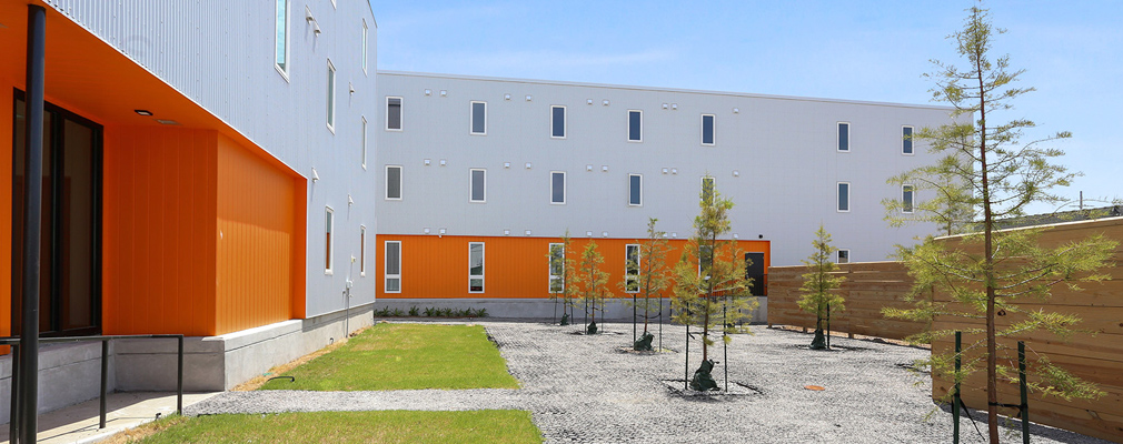 Photograph of a landscaped courtyard framed by two wings of a three-story apartment building and a wood fence.