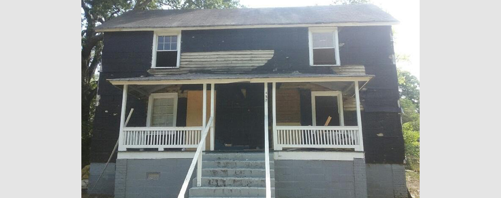 Photograph of the front façade of a dilapidated two-story single-family house.