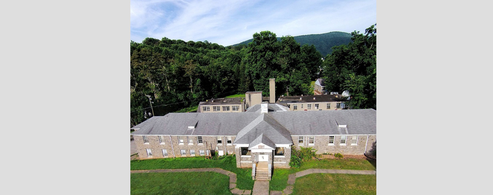 Low-angle aerial photograph of a stone building in front of a parallel brick building, connected by a central hyphen.