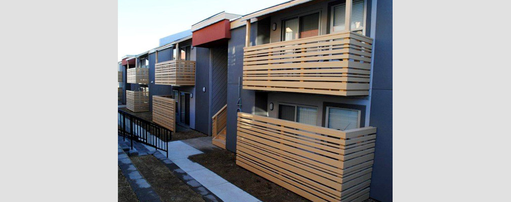 Photograph of the front façade of a two-story apartment building with enclosed private patios and balconies in a modern style.