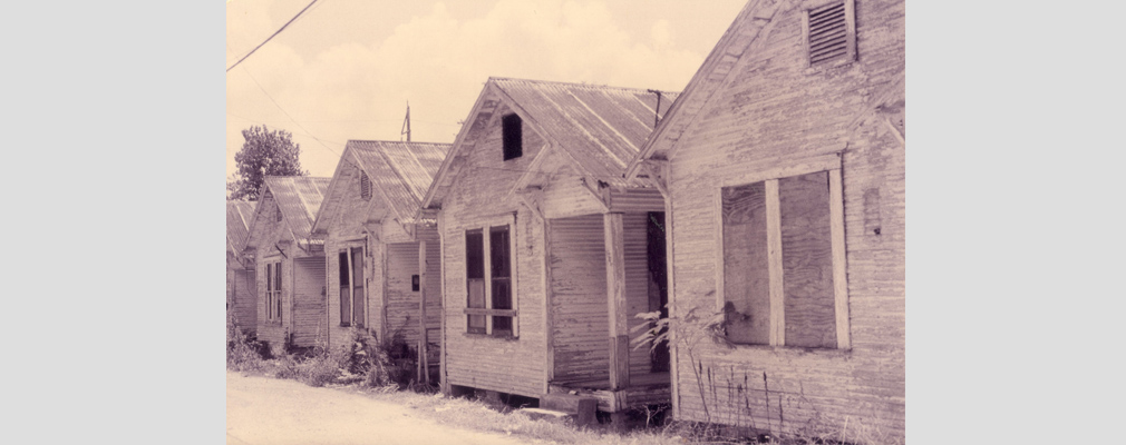 Black and white photograph of the front façades of four wooden shotgun houses.