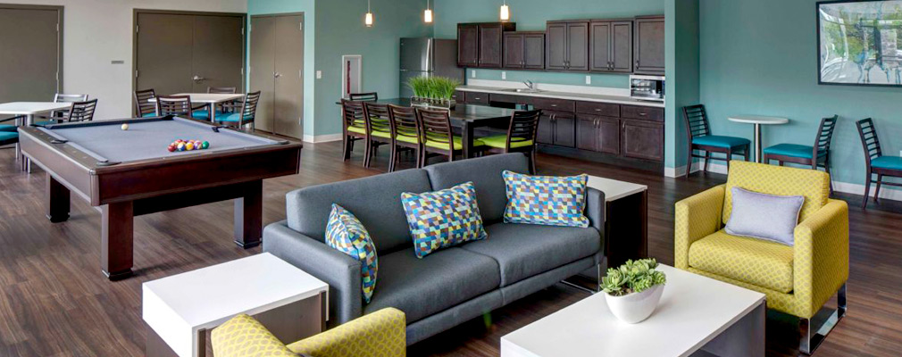 Photograph of a large room with several sets of tables and chairs, a pool table, and a kitchenette.