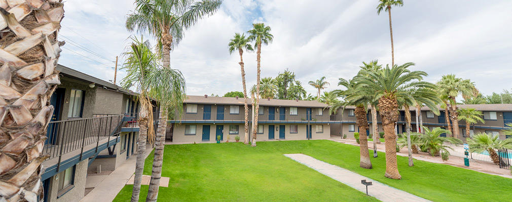 Photograph of a landscaped courtyard from the elevated walkway of a two-story multi-unit residential building enclosing the open space.