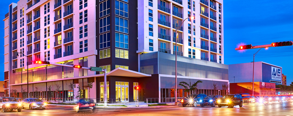 Photograph at night of two façades of a nine-story mixed-use building.