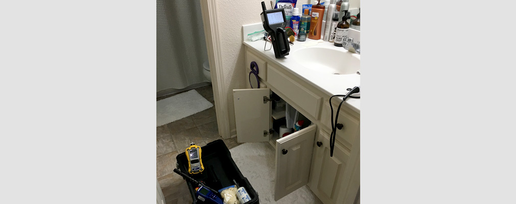 Photograph of a box of environmental measurement equipment on the floor in front of a vanity in a residential bathroom.