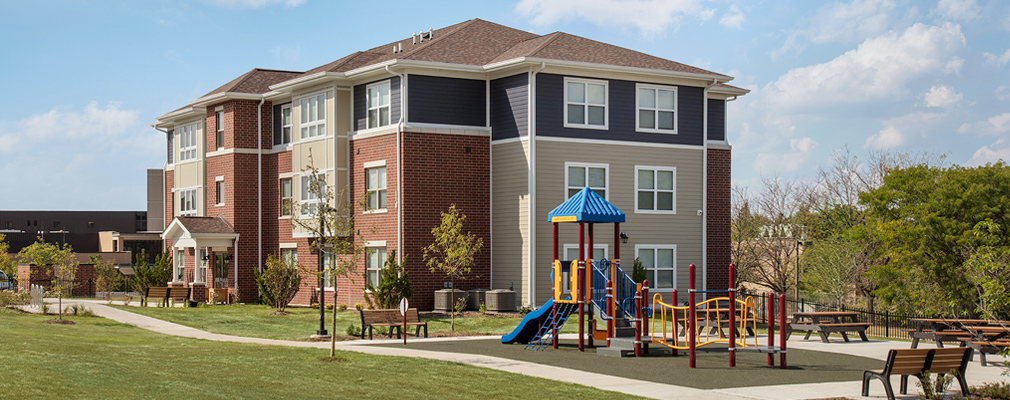 Photograph of a playground, picnic area, and open space adjacent to a three-story residential building. 