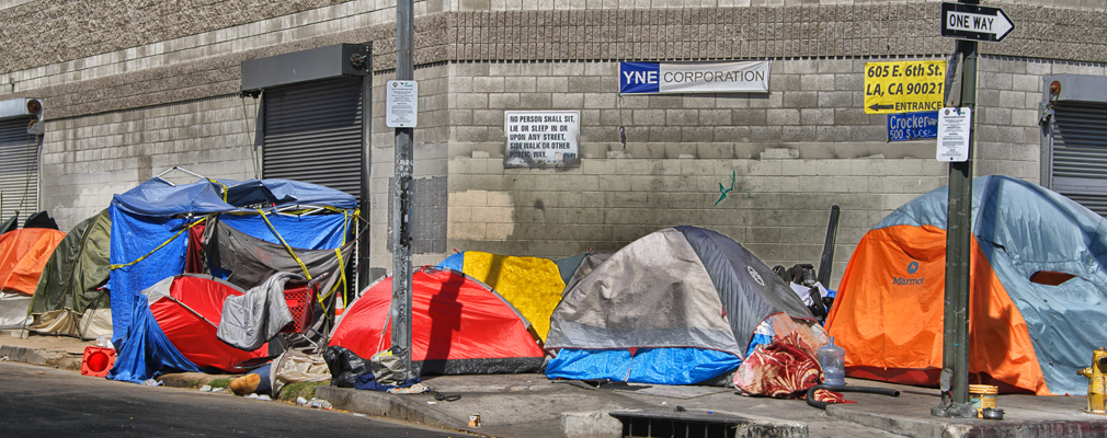 Photograph of several tents placed along a sidewalk at a street intersection.