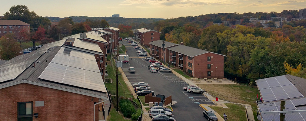 Photograph of solar panels installed on the roof of several brick apartment buildings.