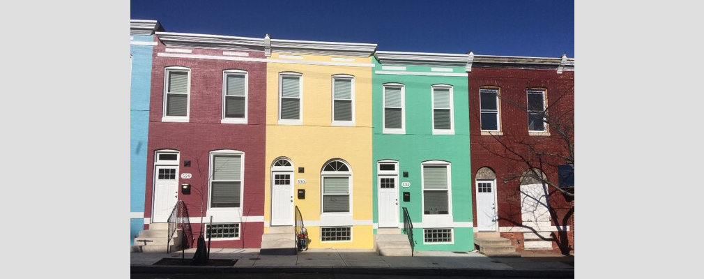 Photograph of the brick façades of freshly painted rowhouses beside an unrehabilitated building on the right edge of the photograph.