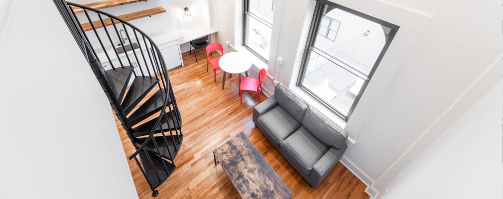 Photograph of the interior of a loft apartment, with a spiral staircase leading down from the loft area to the main floor of the unit.