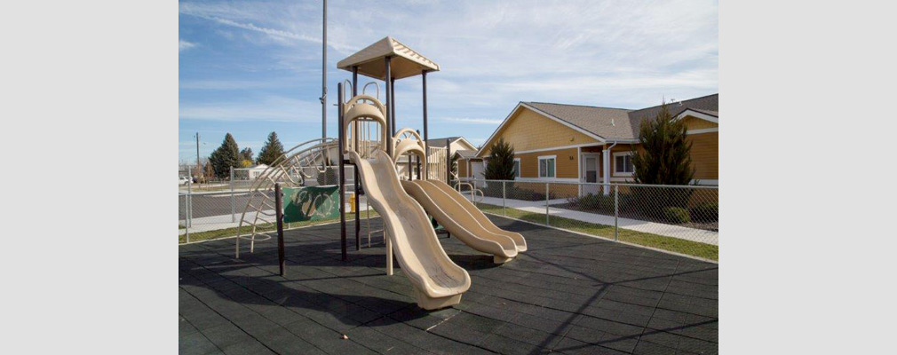 Photograph of a play structure with a single-story duplex in the background.