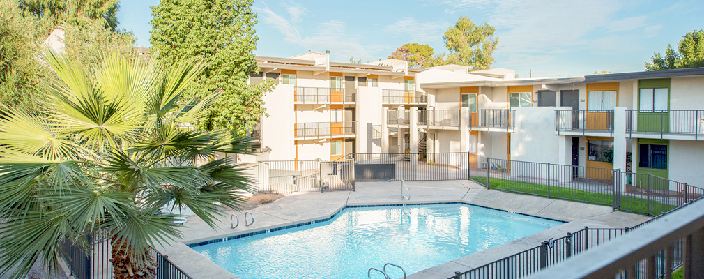 Photograph of a pool in a courtyard taken from the elevated walkway of a two-story multi-unit residential building enclosing the open space.