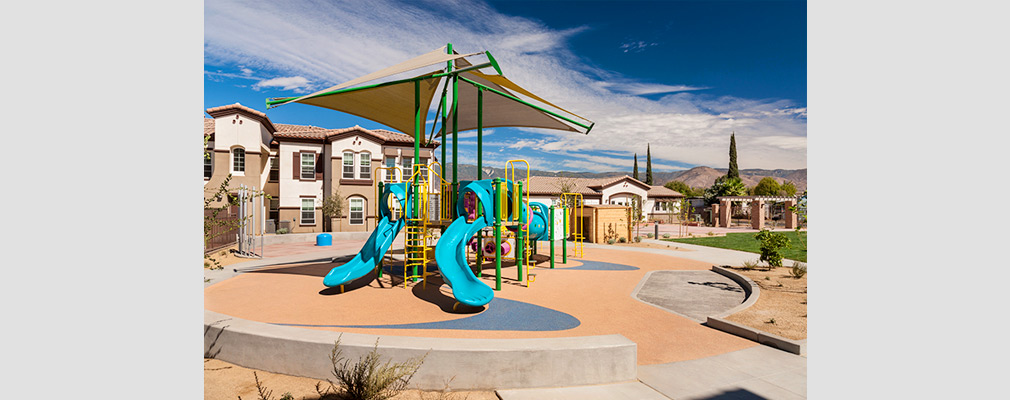 Photograph of a children’s play structure in front of a two-story residential building.