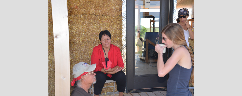 Photograph of four people talking on the porch of the partially-completed straw bale house.